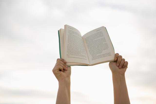 Hands holding an open book against a bright sky, symbolizing freedom, knowledge, and inspiration. Ideal for educational content, reading campaigns, book promotions, and motivational materials.