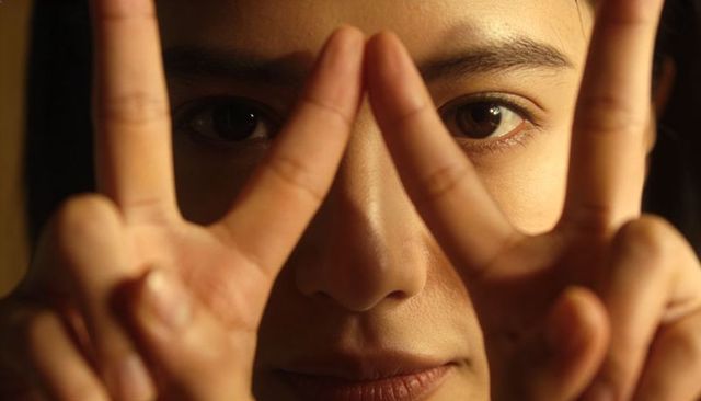 Intimate closeup woman framing face making v-shapes with fingers warm sidelight portrait
