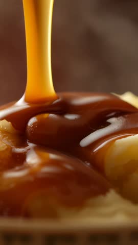 Vertical food video pouring glossy caramel sauce over creamy vanilla ice cream with steam rising