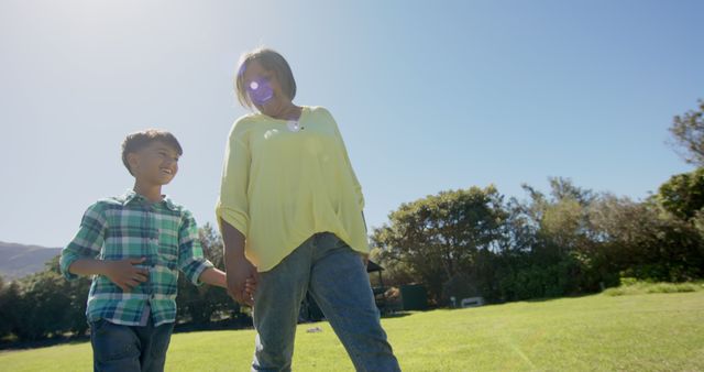 Happy biracial grandmother and grandson walking in sunny garden. Family, togetherness, nature and lifestyle, unaltered.