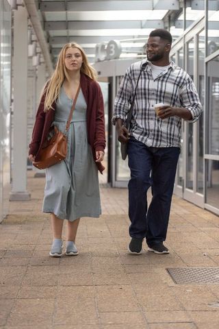 Interracial couple walking through modern transit concourse holding takeaway coffee and crossbody ba