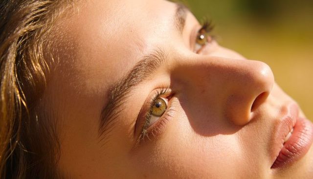 Sunlit closeup of woman gazing with hazel eyes golden hour natural skin and bokeh