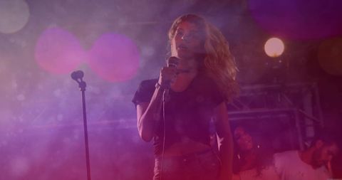 Female vocalist singing on club stage, wired microphone, spotlight haze, colorful bokeh