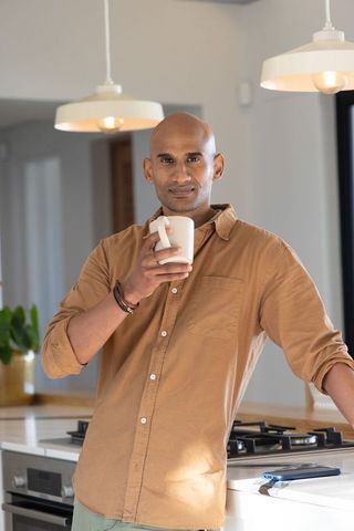 Indian man sipping coffee at modern kitchen counter, minimal interior lifestyle portrait