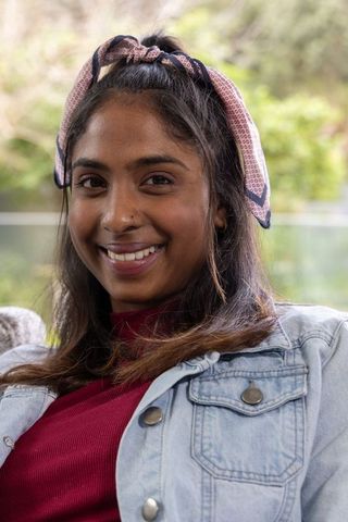 Indian woman smiling on balcony wearing denim jacket and pink headscarf
