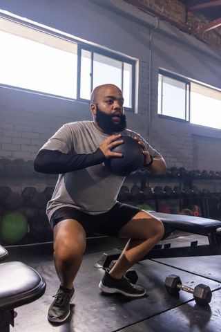 Fit african american man performing weighted squat holding medicine ball in urban gym