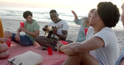 Diverse Friends Relax at Sunset Beach Gathering with Guitar