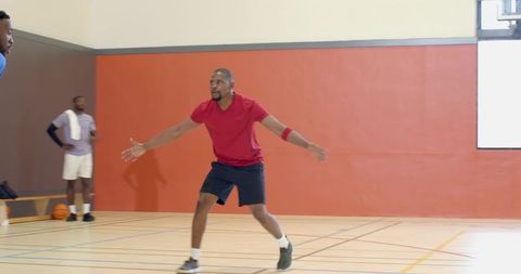 Basketball defender holding low stance on indoor gym court guarding offensive player