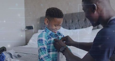 African american father buttoning son's plaid shirt in bedroom showing tender morning bond