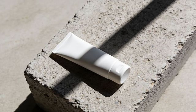 Minimalist white cosmetic tube casting bold shadow on textured concrete backdrop surface