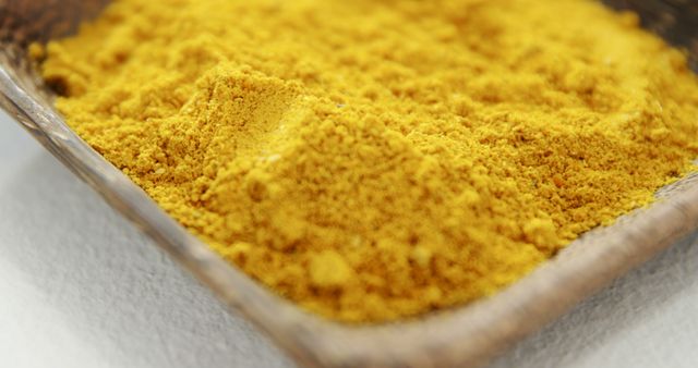 Close-up of turmeric powder in a wooden tray showcasing the vibrant yellow color and fine texture. This image is suitable for use in cooking websites, blogs about natural ingredients, or health-focused articles detailing the benefits of turmeric. Perfect for promoting organic or spice products and culinary magazines.