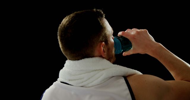 Caucasian man standing backwards and wearing towel and drinking water from water bottle, copy space. Sport, active lifestyle and health concept, unaltered.