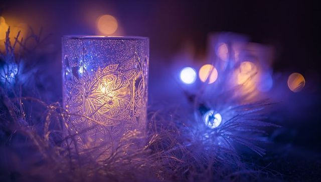 Glowing etched votive casting warm candlelight with blue bokeh and silver tinsel decor
