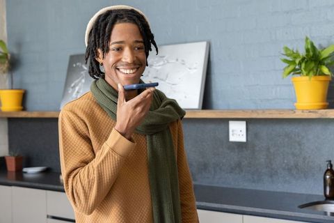 Young African American man speaking into smartphone while smiling in contemporary kitchen
