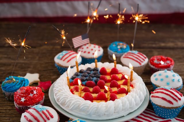Patriotic 4th of July cake and cupcakes decorated with red, white, and blue colors, topped with sparklers and an American flag. Ideal for celebrating Independence Day, holiday parties, and summer gatherings. Perfect for use in festive event promotions, holiday-themed advertisements, and social media posts celebrating American patriotism.