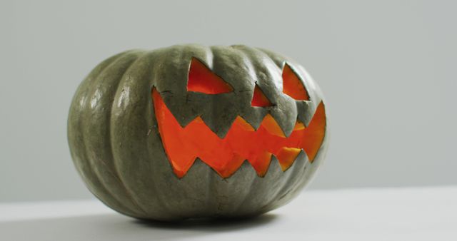Grey pumpkin carved with a scary Jack-O'-Lantern face, glowing brightly from within. Ideal for Halloween themes, spooky decorations, autumn celebrations, and themed displays.