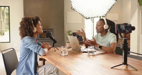 Black women recording podcast at home studio table with microphone, laptop and camera
