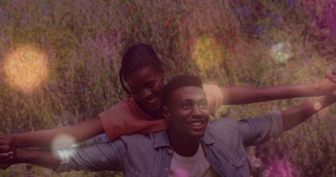 Young couple sharing piggyback joy, laughing and balancing arms in sunny meadow with bokeh