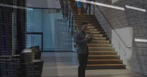 Mature businessman standing in modern lobby holding tablet with software code overlay
