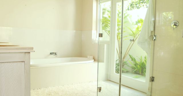 This image features a modern bathroom with a luxurious bathtub next to a glass door opening to a garden. Perfect for use in interior design websites, home decor blogs, and real estate listings highlighting modern and elegant bathroom designs. Ideal for wellness and relaxation content showcasing a serene and spacious bathing area.