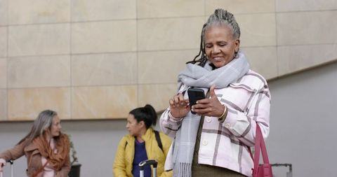 Senior african american woman using smartphone on train concourse with luggage and scarf