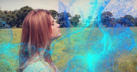 Young woman standing in meadow with eyes closed surrounded by turquoise particle swirl