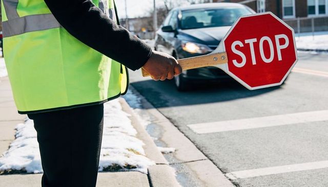 Crossing guard holding stop paddle directing traffic at snowy urban crosswalk