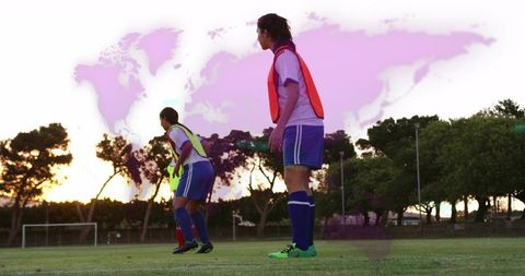 Women soccer players standing at sunset wearing training bibs with purple world map sky