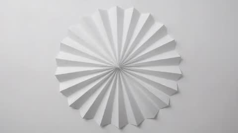 Rotating White Paper Rosette Casting Dynamic Radial Shadows on Minimal Gray Wall