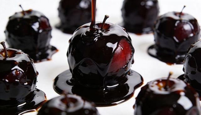 Drizzling dark chocolate glaze over ripe red cherries, coating glossy gourmet confections