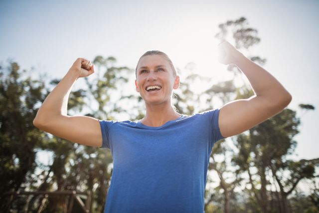 Fit woman cheering in joy during an outdoor boot camp, showcasing strength and motivation. Ideal for promoting fitness programs, healthy lifestyle campaigns, and motivational content. The natural background with sunlight and trees adds a refreshing and energetic vibe.