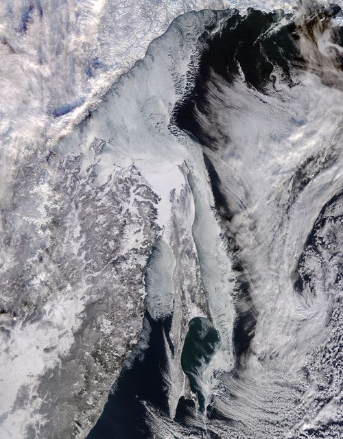 This detailed satellite image showcases the ice-covered Sea of Okhotsk off Russia's east coast, captured by NASA's Terra satellite in January 2015. The image emphasizes the effects of Siberian winds, cold temperatures, and fresh water from the Amur River on seasonal ice formation. Ideal for environmental studies, climate change discussions, and geographical education.