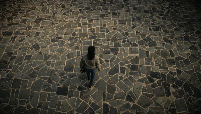Woman walking across irregular mosaic stone plaza from overhead holding smartphone