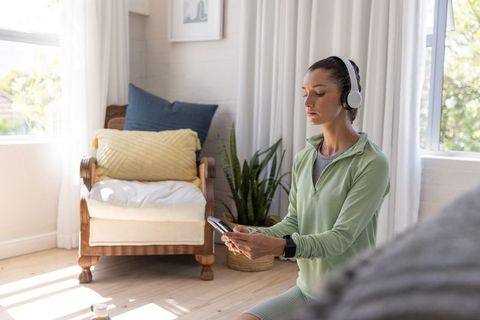 Woman using smartphone and headphones preparing home workout in sunlit living room