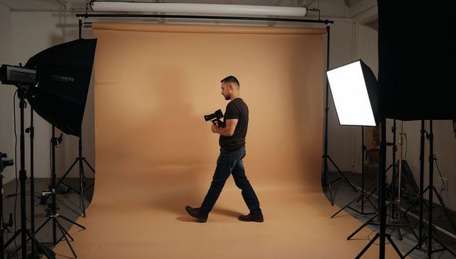 Male photographer walking through studio holding dslr amid professional lighting gear