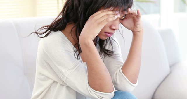 A young woman appears distressed or overwhelmed, with her hands on her forehead in a gesture of worry or headache. Her expression and body language suggest she may be dealing with stress or emotional pain.