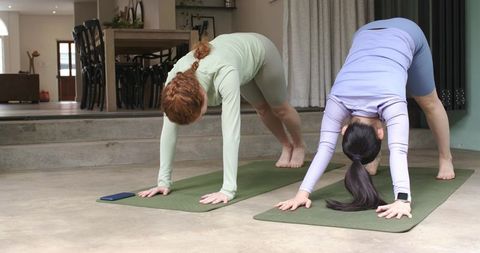 Women Practicing Downward Dog on Green Mats in Modern Home with Fitness Tracker and Phone