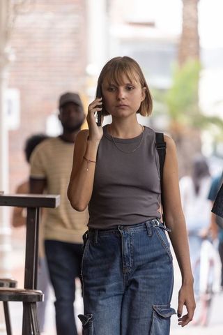 Young woman walking and talking on smartphone wearing jeans and tank top, urban backpack