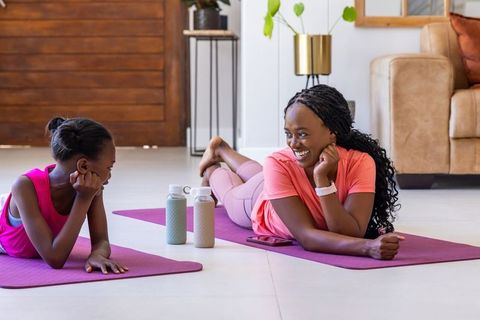 Mother and teen daughter doing mat exercises at home smiling and stretching together