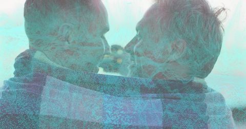 Mature gay couple embracing under blue plaid blanket at shoreline, teal double exposure