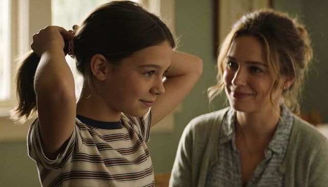 Preteen girl tying ponytail while mother smiling nearby warm home morning family moment