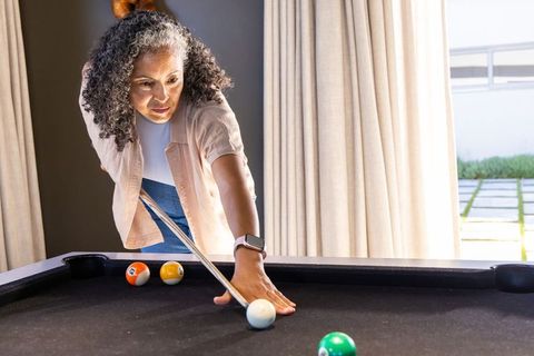 Senior african woman lining up pool shot wearing smartwatch in sunlit lounge