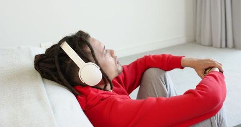 Relaxing man with dreadlocks listening to music on headphones in minimalist apartment