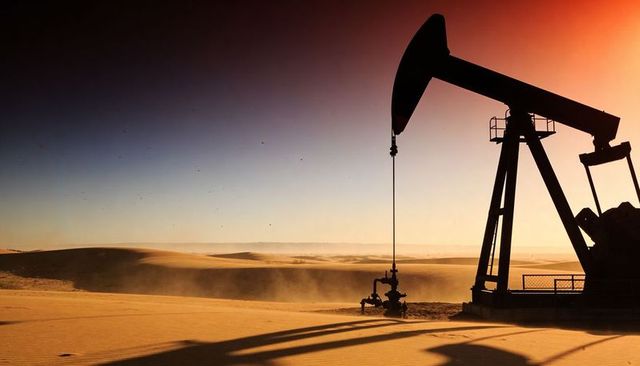 Desert pumpjack silhouette at sunrise casting long shadows across dunes
