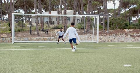 Boys Playing Soccer on Turf Field Under Pine Trees