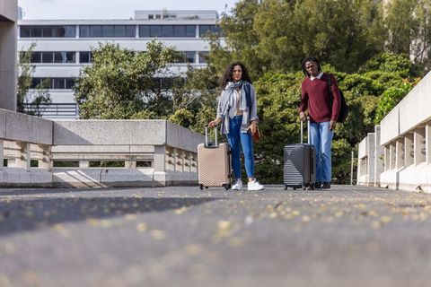 Young couple standing with rolling luggage on urban bridge preparing for travel
