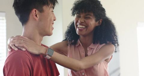 Multiracial couple laughing and embracing at home with smartwatch and ring, sunlit