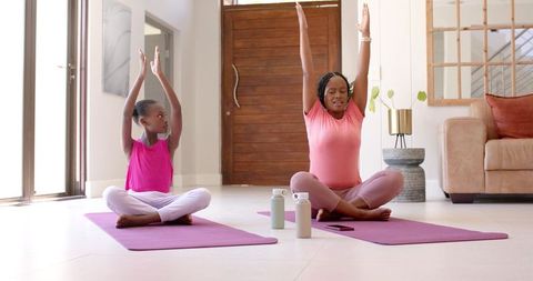 African american mother and daughter practicing yoga and stretching at home on purple mats