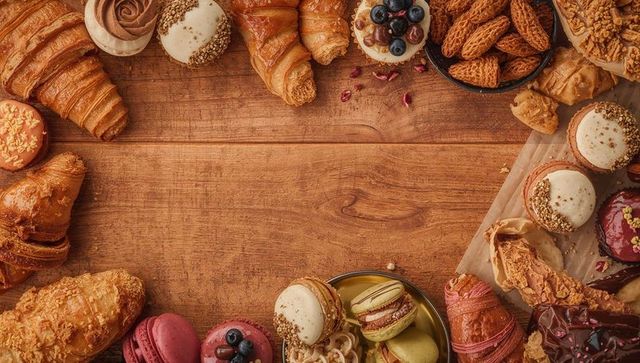 Showcasing assorted croissants and colorful macarons on rustic wooden tabletop flatlay