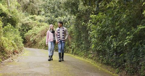 Couple walking mossy forest trail wearing sweaters scarves beanie and rubber boots